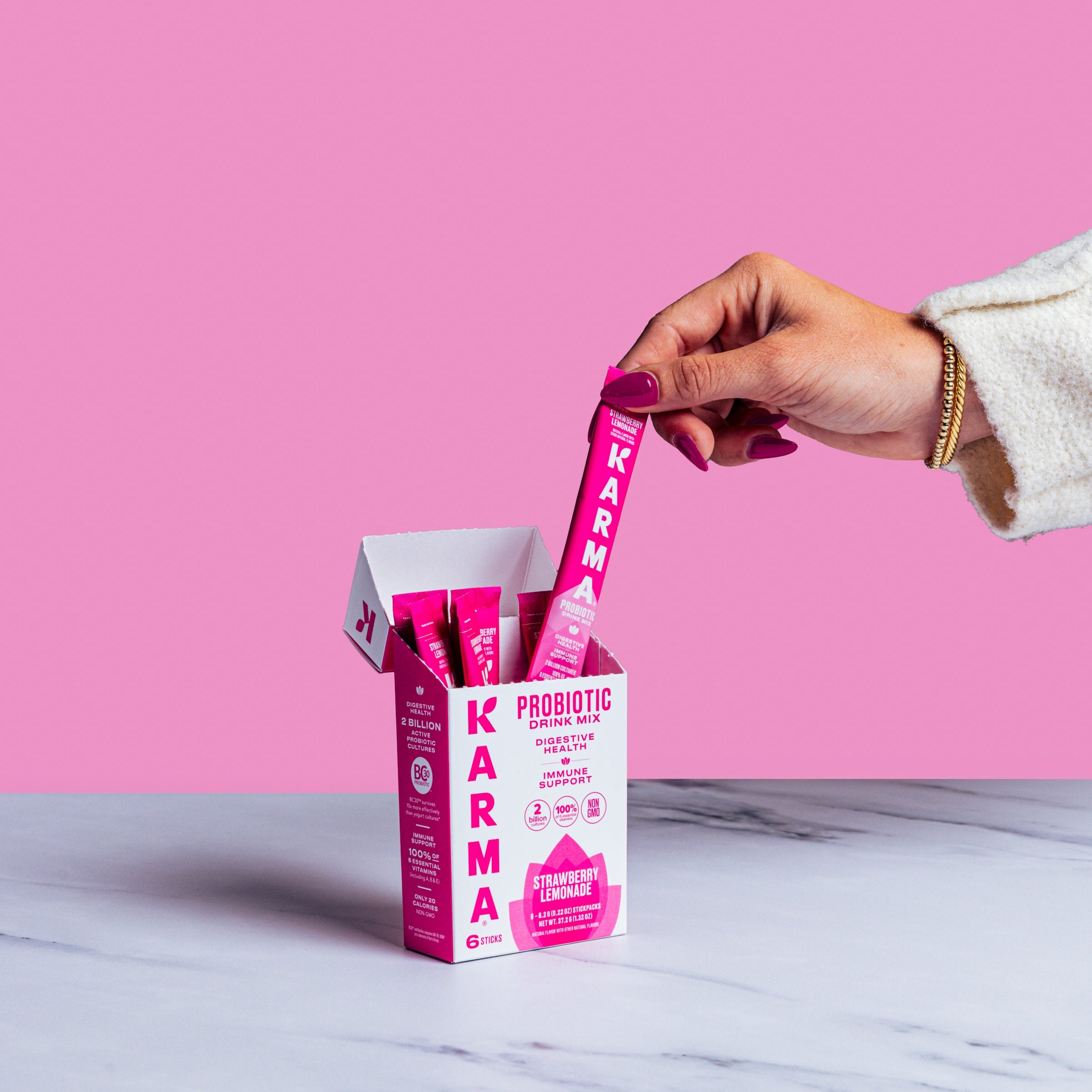 Hand picking a pink Karma Probiotic stick from a box on a marble surface with pink background
