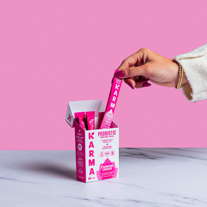 Hand picking a pink Karma Probiotic stick from a box on a marble surface with pink background